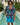 Man wearing a colorful floral shirt and blue shorts standing by a pool with palm trees in the background