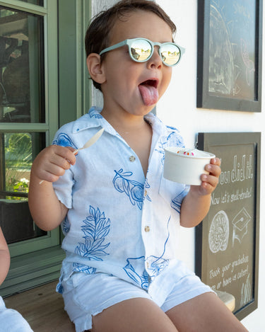 Child in a light blue outfit with floral patterns eating ice cream outdoors.