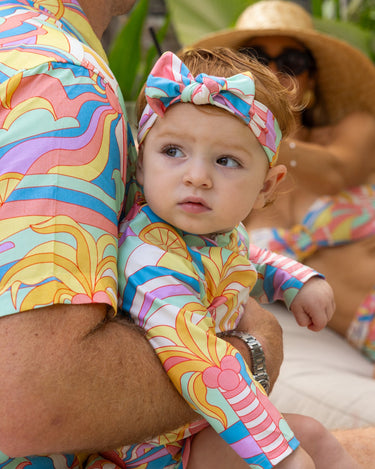 Man and woman in colorful matching outfits with a baby in a matching outfit on vacation.