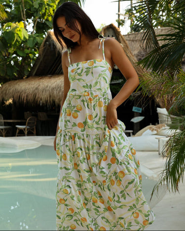 Woman in a floral dress standing by a pool with tropical plants and a hut in the background